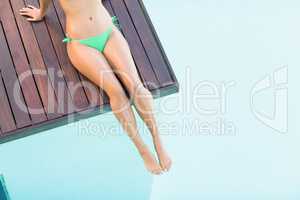 Beautiful woman in green bikini relaxing on wooden deck by pools