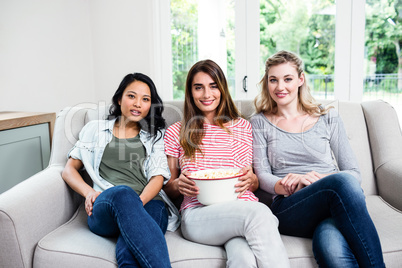 Happy young female friends with popcorn at home