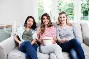 Happy young female friends with popcorn at home