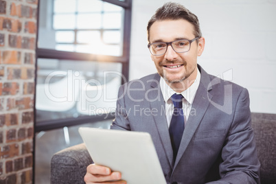 Portrait of smiling businessman holding digital table while sitt