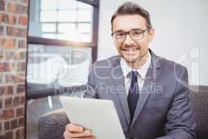 Portrait of smiling businessman holding digital table while sitt