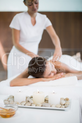 Candles and pebbles in tray while woman and masseur in backgroun