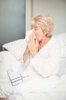 Senior woman covering nose while sneezing in bedroom