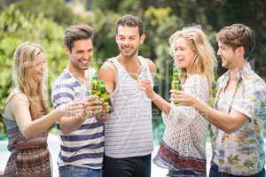 Group of friends toasting beer bottles near pool