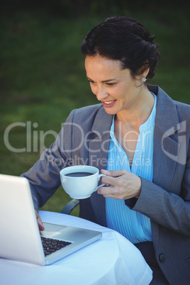 Pretty businesswoman using laptop and having coffee