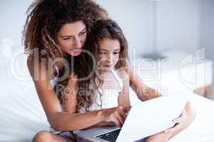 Mother and daughter using laptop on bed