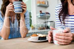 Midsection of female friends holding coffee mugs