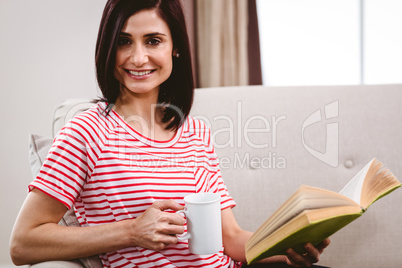 Portrait of smiling woman holding book and coffee mug