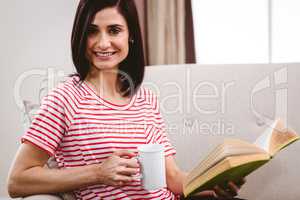 Portrait of smiling woman holding book and coffee mug