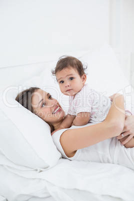 Mother holding baby girl while lying on bed