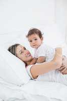 Mother holding baby girl while lying on bed
