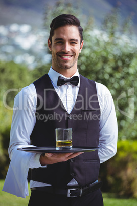 Handsome waiter holding a tray with glass of whiskey