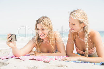 Two friends taking selfie while lying on the beach