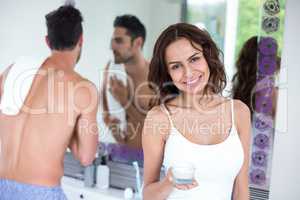 Happy woman holding cream while husband in background