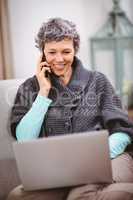 Smiling mature woman with laptop using mobile phone