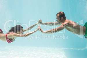 Couple holding hands while swimming underwater