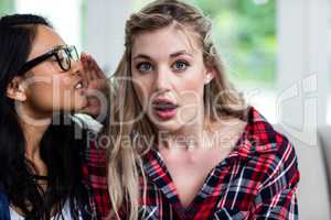 Young woman whispering to female friend