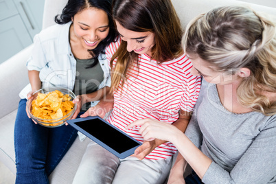 Female friends looking in digital tablet while having snacks