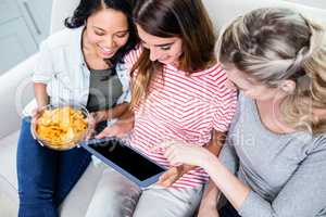 Female friends looking in digital tablet while having snacks