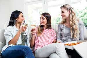 Female friends with pizza drinking wine at home