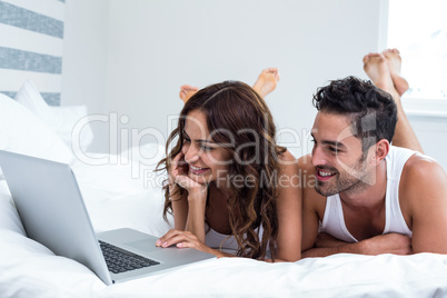 Smiling couple using laptop while lying under blanket