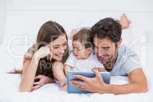 Young family looking at digital tablet on bed