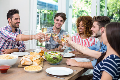 Young friends toasting wine while having meal at table