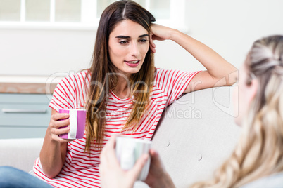 Beautiful woman talking with female friend while drinking coffee