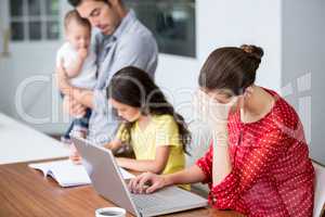 Tensed mother working on laptop with father helping daughter in