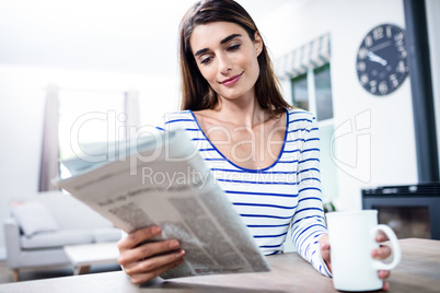 Woman reading newspaper while holding mug