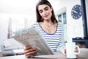 Woman reading newspaper while holding mug