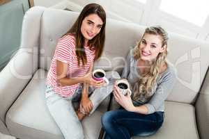 Portrait of female friends drinking coffee on sofa