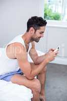 Young man using mobile phone while sitting on bed