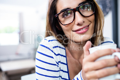 Contemplated young woman smiling while holding coffee