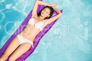 Beautiful woman in white bikini relaxing on air bed in pool