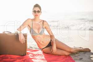Glamorous woman in bikini sitting next to suitcase on the beach