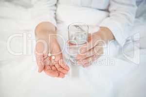 Woman holding pills and drinking glass