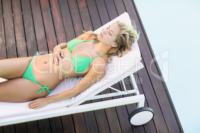 Beautiful woman in green bikini relaxing by poolside