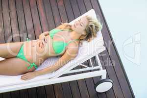 Beautiful woman in green bikini relaxing by poolside