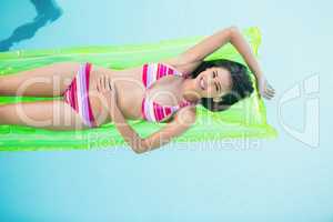 Happy woman in bikini lying on air bed in swimming pool