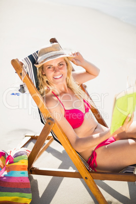 Woman in bikini sitting on armchair and reading book