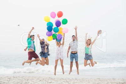 Group of friends jumping on the beach with balloons