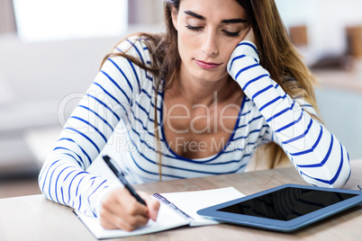Young woman writing in notepad while sitting at table