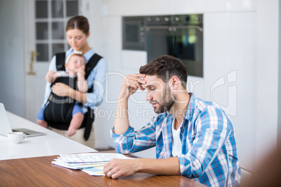 Man looking in documents while wife and baby in background