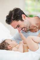 Close-up of smiling father playing with baby on bed