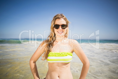 Pretty woman in bikini and sunglasses standing on the beach