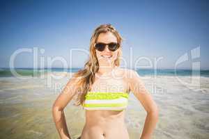 Pretty woman in bikini and sunglasses standing on the beach