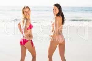 Two happy women standing on the beach with hand on hip