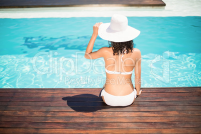 Rear view of woman wearing white bikini and hat sitting near poo