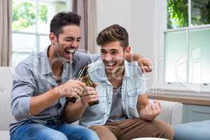 Male friends toasting beer while sitting on sofa